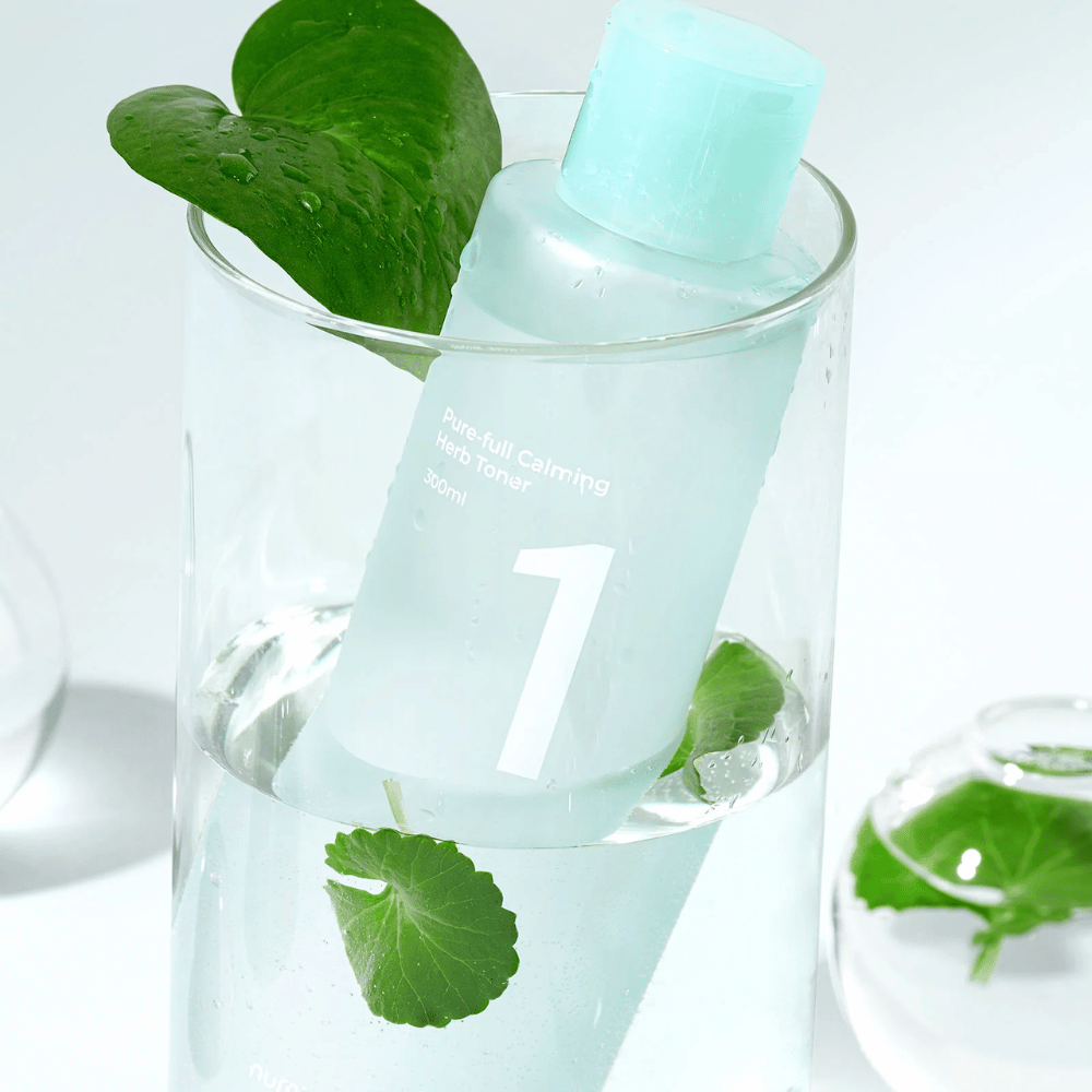 Een fles met No.1 Pure-Full Calming Herb Toner geplaatst in een glas met water en groene bladeren. De fles heeft een lichtblauwe dop en een etiket met de tekst "Pure-full Calming Herb Toner" en "300ml". Het product ziet er fris uit met water en groen op de achtergrond, wat een kalmerend en natuurlijk gevoel geeft.