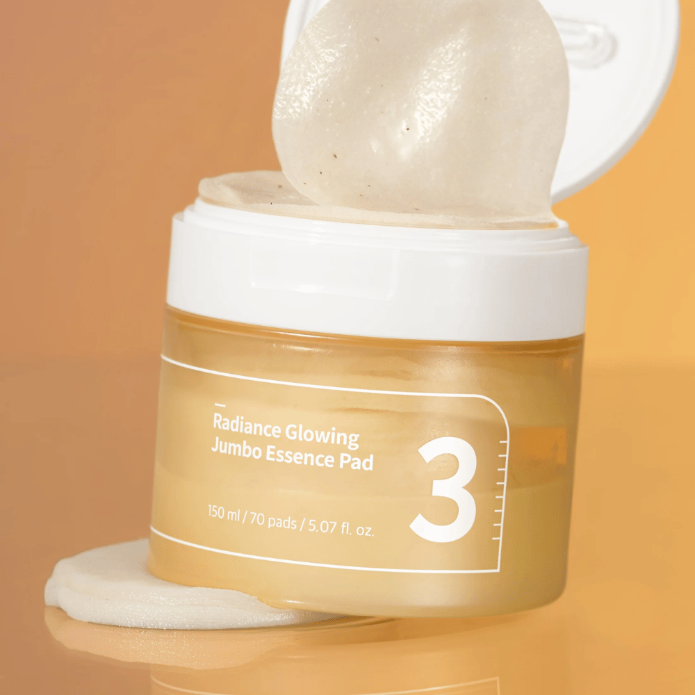 Open pot met numbuzin No. 3 Radiance Glowing Jumbo Essence Pad, een pad is zichtbaar leunend tegen de rand, achtergrond in oranje tint.