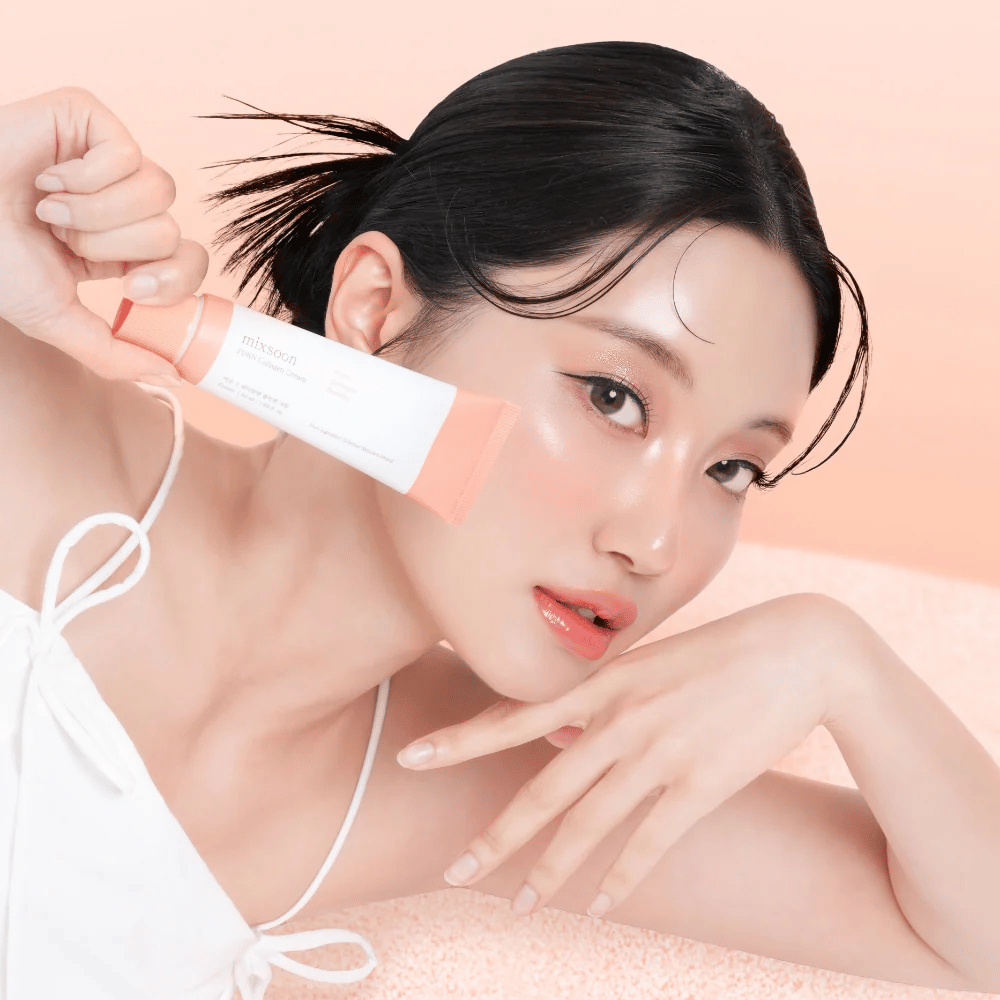 Persoon met stralende huid houdt Mixsoon PDRN Collagen Cream dicht bij de wang. De crème hydrateert, versterkt de elasticiteit en geeft een frisse glow.