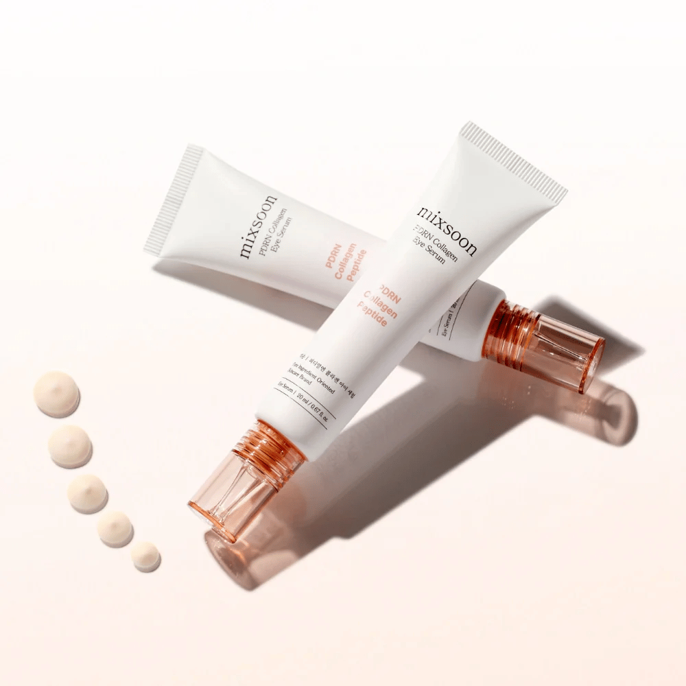 Twee tubes van Mixsoon PDRN Collagen Eye Serum liggen gekruist met kleine druppels van het serum. Een lichte oogbehandeling die hydrateert en lijntjes verzacht.