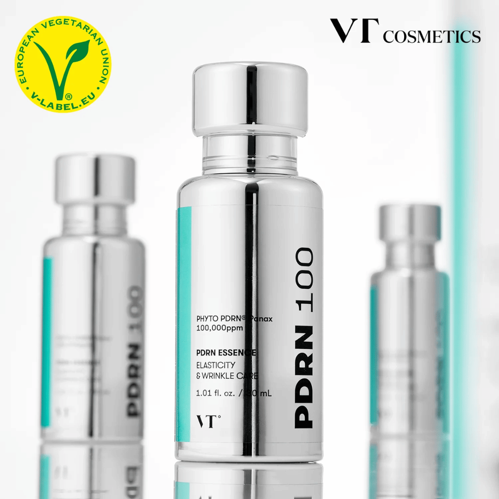 Meerdere zilverkleurige flessen van VT PDRN 100 Essence staan op een rij, met duidelijke markering van 100.000 ppm PDRN en focus op elasticiteit en rimpelverzorging. Bovenaan is het logo van VT Cosmetics zichtbaar en een V-label voor vegetarische inhoud.