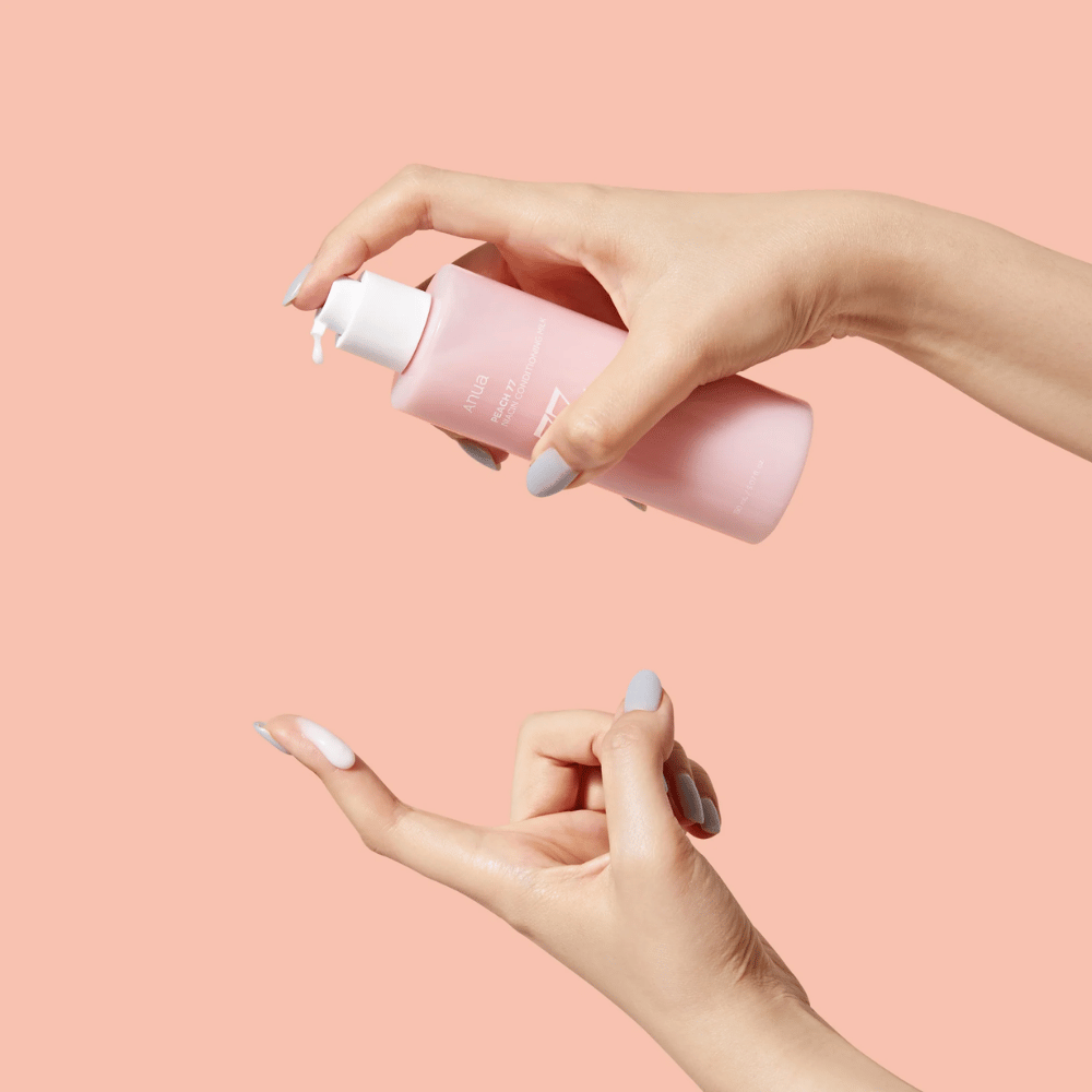De afbeelding toont iemands handen die een fles vasthouden met ANUA Peach 77% Niacin Conditioning Milk. Dit huidverzorgingsproduct lijkt een melkachtige consistentie te hebben en is ontworpen om de huid te verzorgen en te verbeteren.