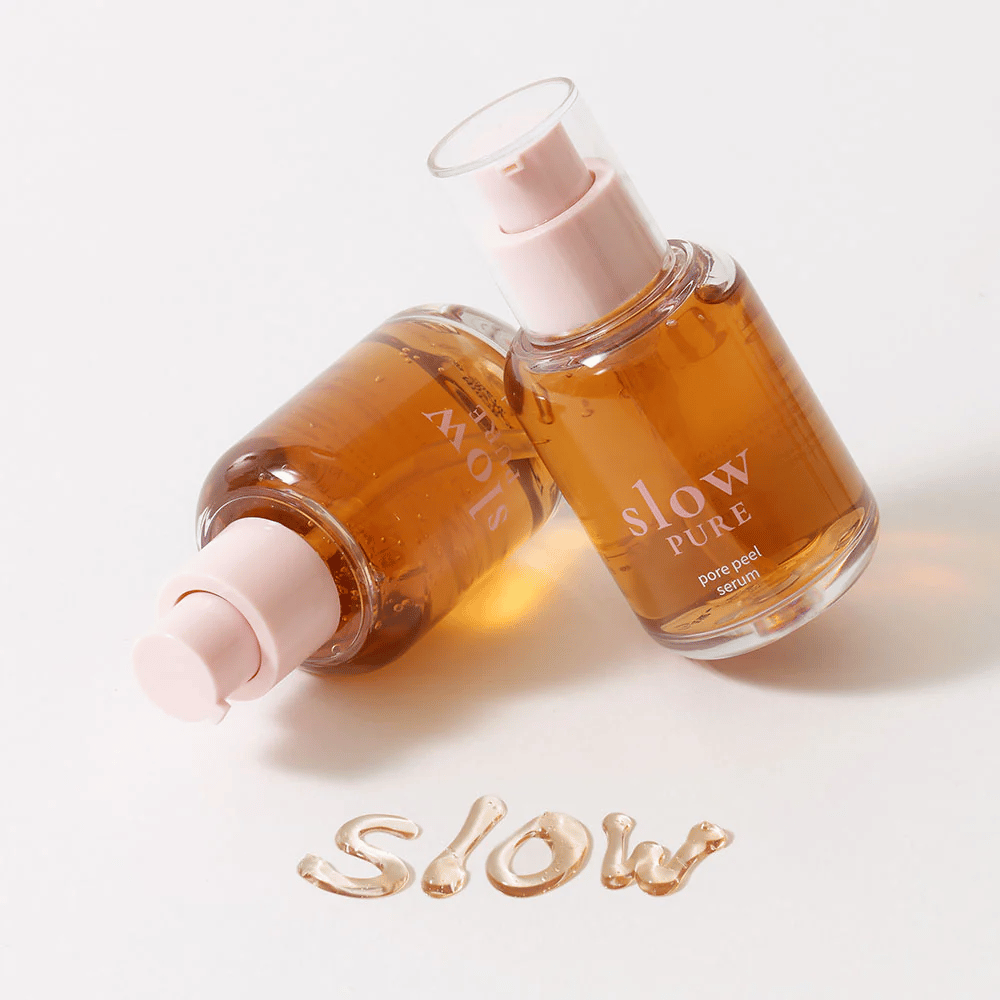 Twee flessen Slow Pure Pore Peel Serum met pomp, tekst geschreven in serum op het oppervlak: "Slow".