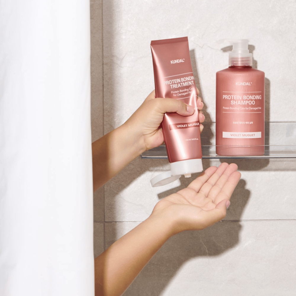 KUNDAL Protein Bonding Treatment Violet Muguet gebruikt in de douche, met Protein Bonding Shampoo geplaatst op de plank ernaast.