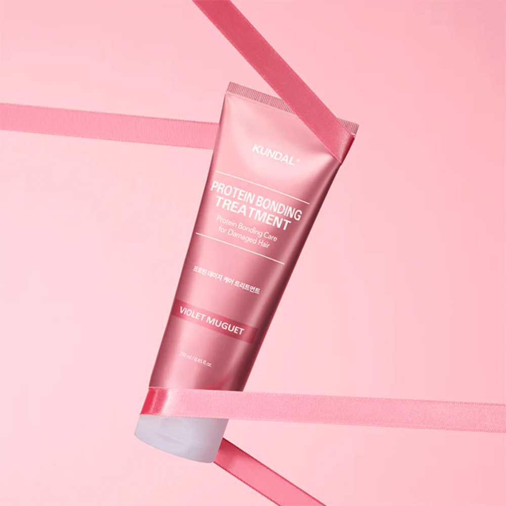 KUNDAL Protein Bonding Treatment Violet Muguet in roze tube 250 ml tegen roze achtergrond met decoratieve linten.