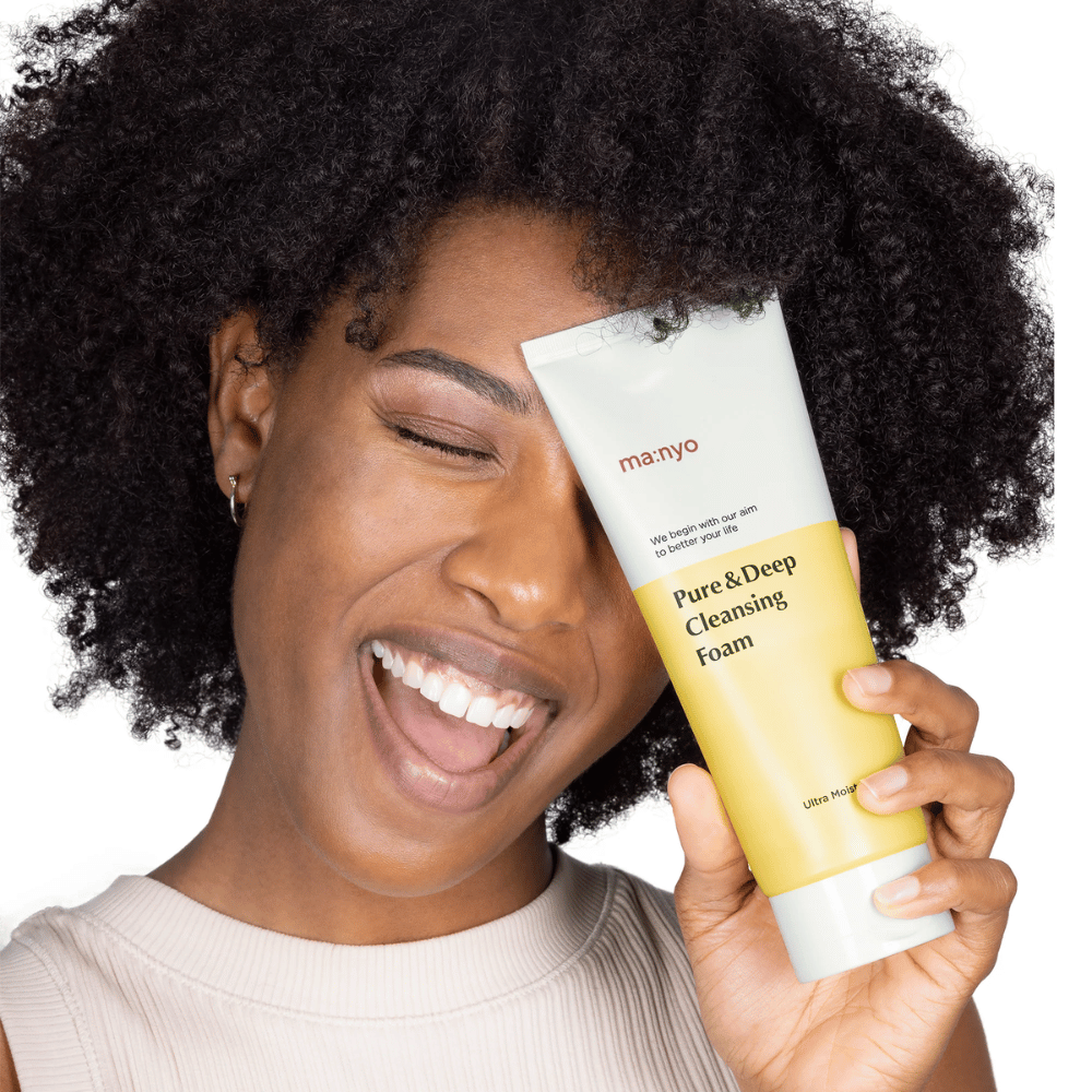 Vrouw met krullend haar houdt Ma:nyo Pure & Deep Cleansing Foam – een milde Koreaanse reiniger die effectief vuil en make-up verwijdert zonder de huid uit te drogen.