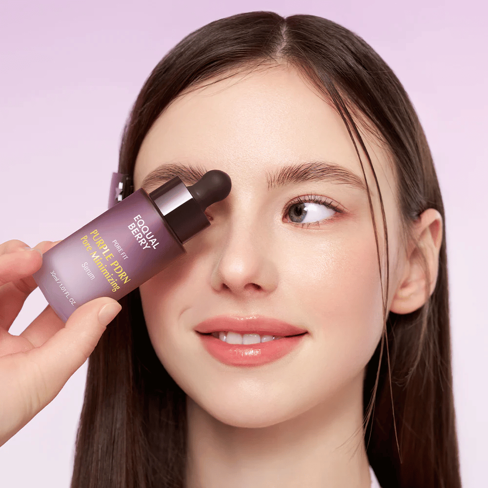 Jonge vrouw met een gladde huid houdt een fles Equal Berry Purple PDRN Pore Minimizing Serum tegen haar voorhoofd, tegen een lichtpaarse achtergrond.