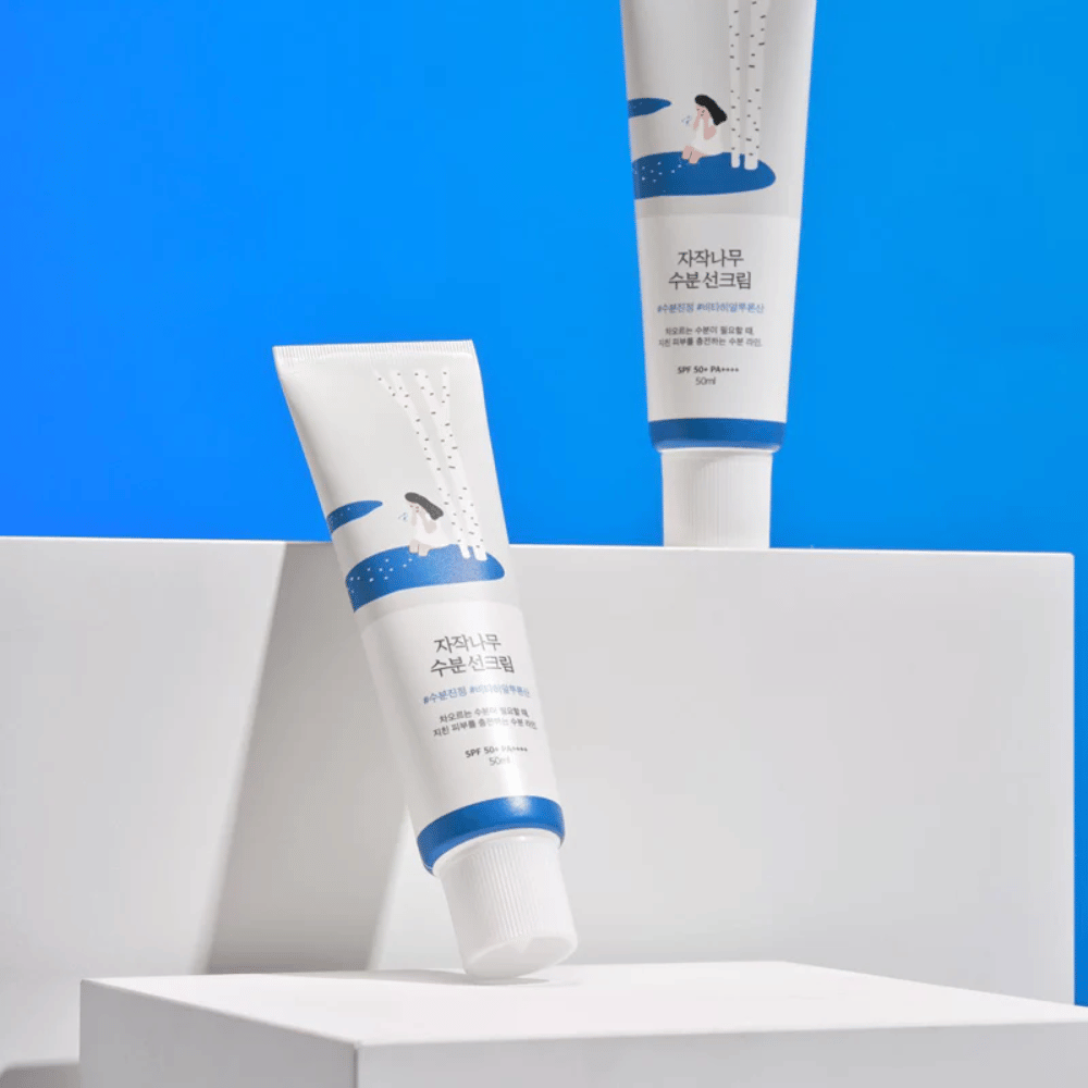 Twee tubes met Round Lab Birch Juice Moisturizing Sunscreen SPF50+ PA++++ 50ml die op een blauwe achtergrond staan.