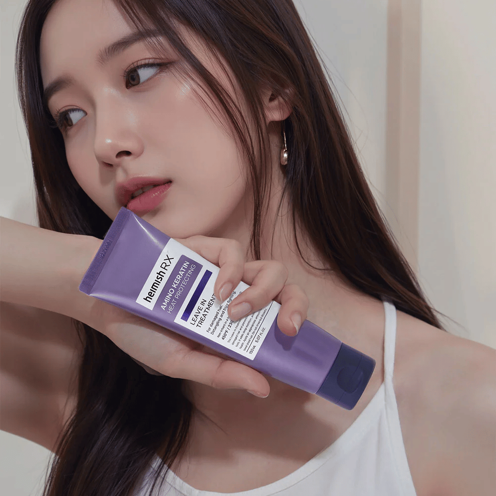 Vrouw met lang, glanzend haar houdt Heimish RX Amino Keratin Leave-In Treatment vast - toont het product als een verzorgende en hittebeschermende stap in de haarverzorgingsroutine.