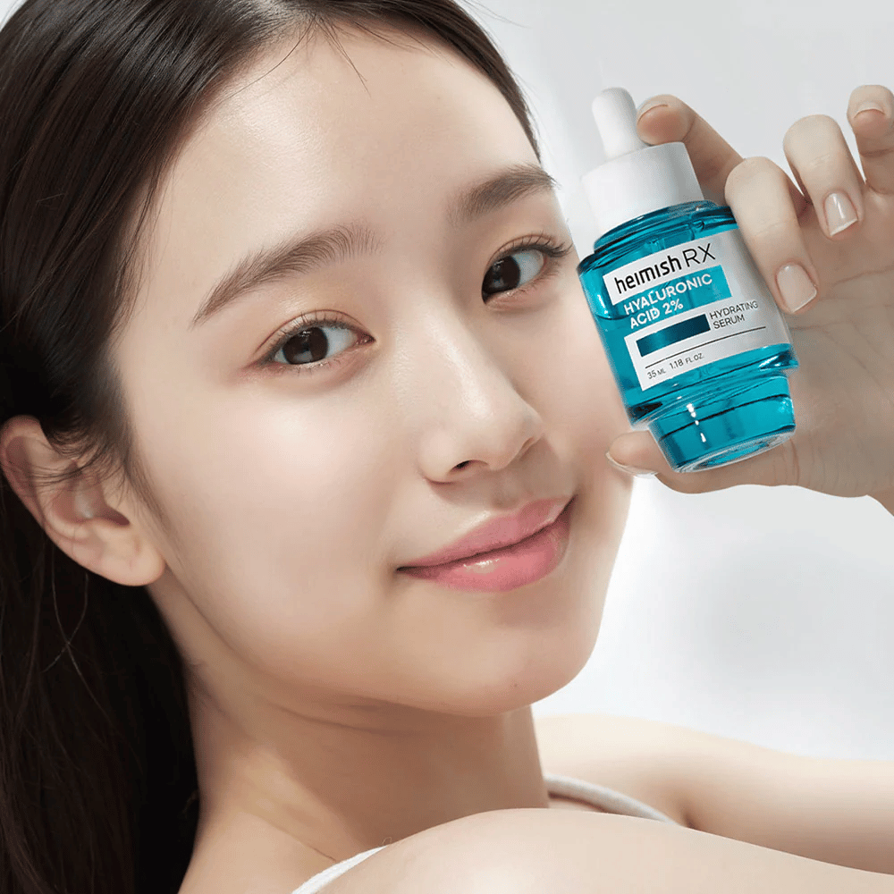 Lachende vrouw met stralende huid houdt een fles Heimish RX Hyaluronic Acid 2% Hydrating Serum vast, wat de hydraterende eigenschappen benadrukt.