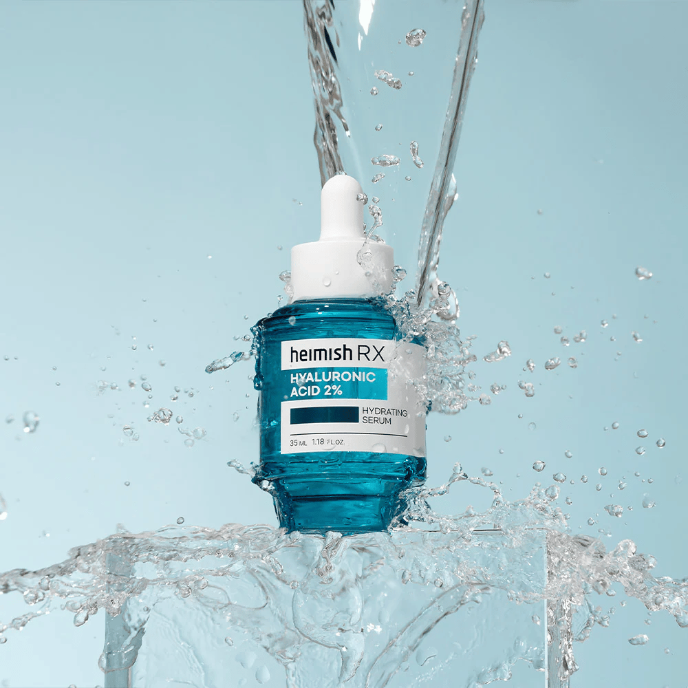 Heimish RX Hyaluronic Acid 2% Hydrating Serum geplaatst op een ijsachtige ondergrond met water dat rond spat, wat intense hydratatie en frisheid symboliseert.