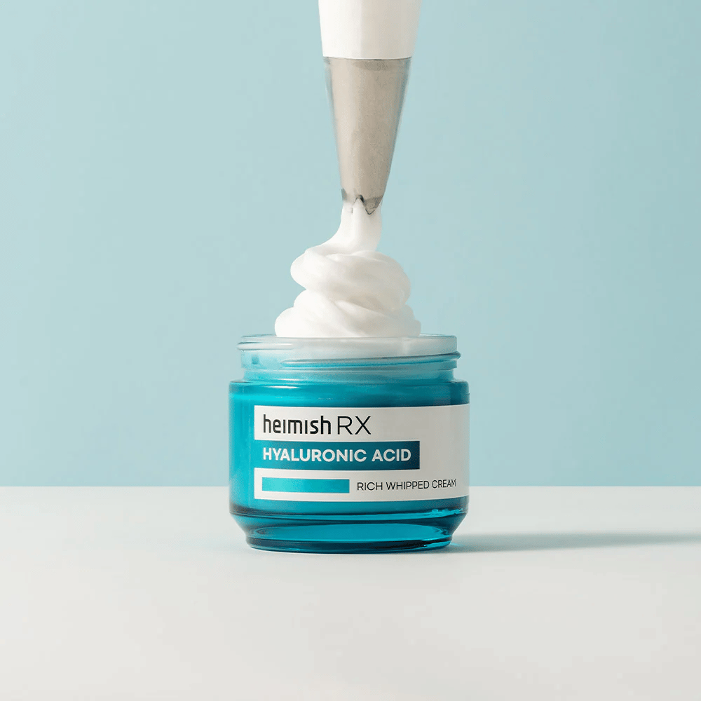 Heimish RX Hyaluronic Acid Rich Whipped Cream in een blauwe glazen pot, waar een spuitzak de luchtige crème aanbrengt. Een hydraterende gezichtscrème met hyaluronzuur voor intensieve hydratatie en een zachte, volle huid.