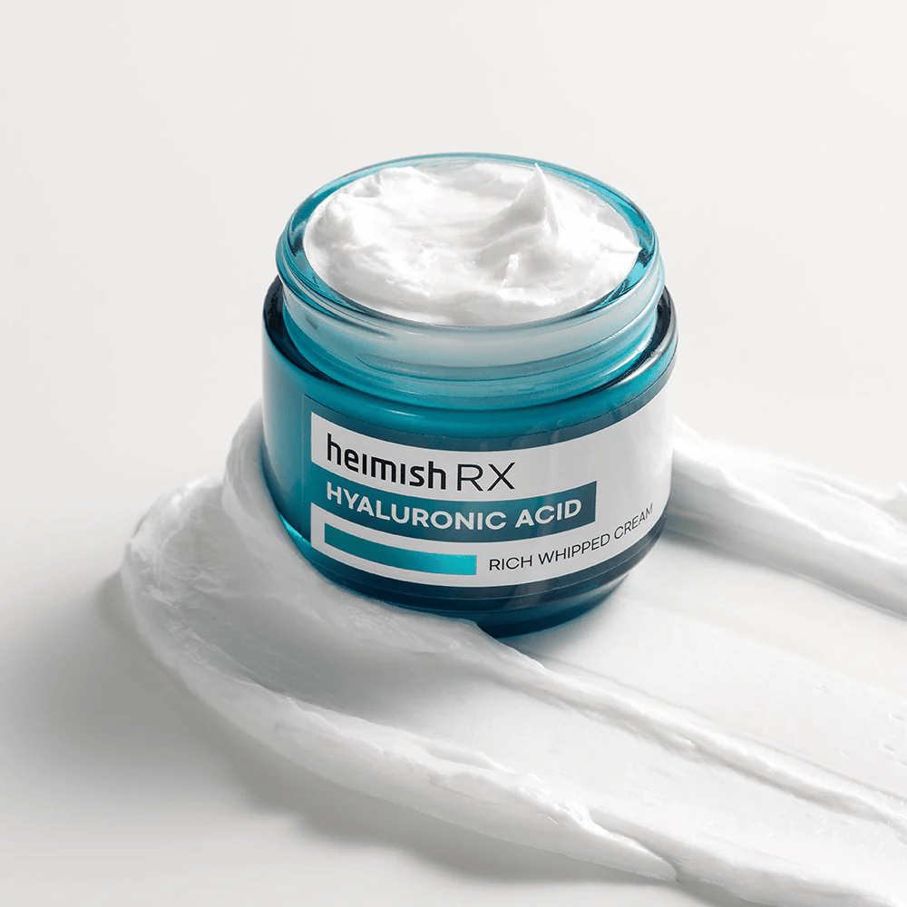 Heimish RX Hyaluronic Acid Rich Whipped Cream in een blauwe glazen pot met rijke en luchtige textuur, verspreid op een witte achtergrond. Intens hydraterende gezichtscrème met hyaluronzuur voor diepe hydratatie en zachte huid.
