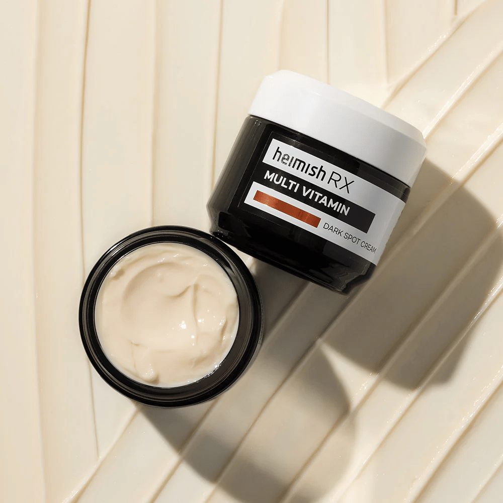 heimish RX Multi Vitamin Dark Spot Cream – een voedende gezichtscrème om donkere vlekken te verminderen en de huid een egalere tint te geven. De zachte textuur van de crème wordt getoond in een open pot met een elegante verpakking.