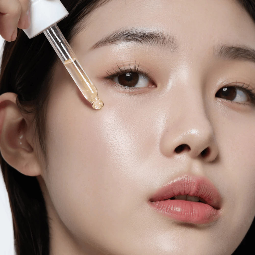 Close-up van een vrouw met gladde, gehydrateerde huid die Heimish RX Multi Vitamin 7% Glow Serum aanbrengt met een pipet voor extra glans en voeding.