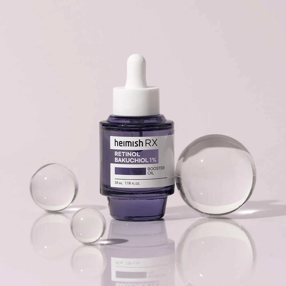 Heimish RX Retinol Bakuchiol Booster Oil 1% in een elegante paarse glazen fles met pipet. De olie is geplaatst op een reflecterend oppervlak met glazen kralen eromheen, wat een luxe en moderne uitstraling geeft.
