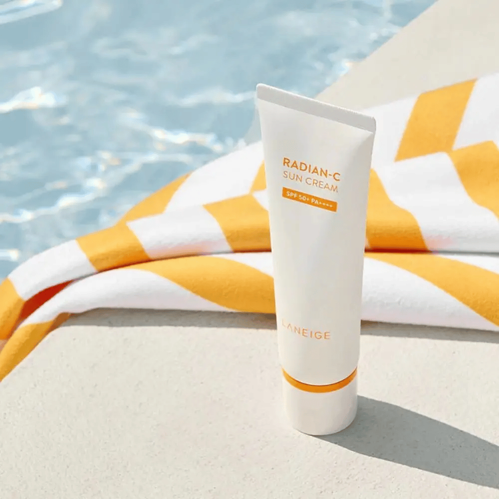 LANEIGE Radian-C Sun Cream staat bij de rand van een zwembad met een geel-wit gestreepte handdoek op de achtergrond.