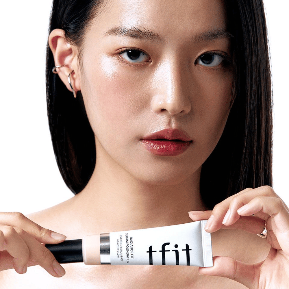 Model met glanzende, gladde huid houdt TFIT Radiance Fit Serum Foundation vast, wat de natuurlijke finish en glans van het product benadrukt.