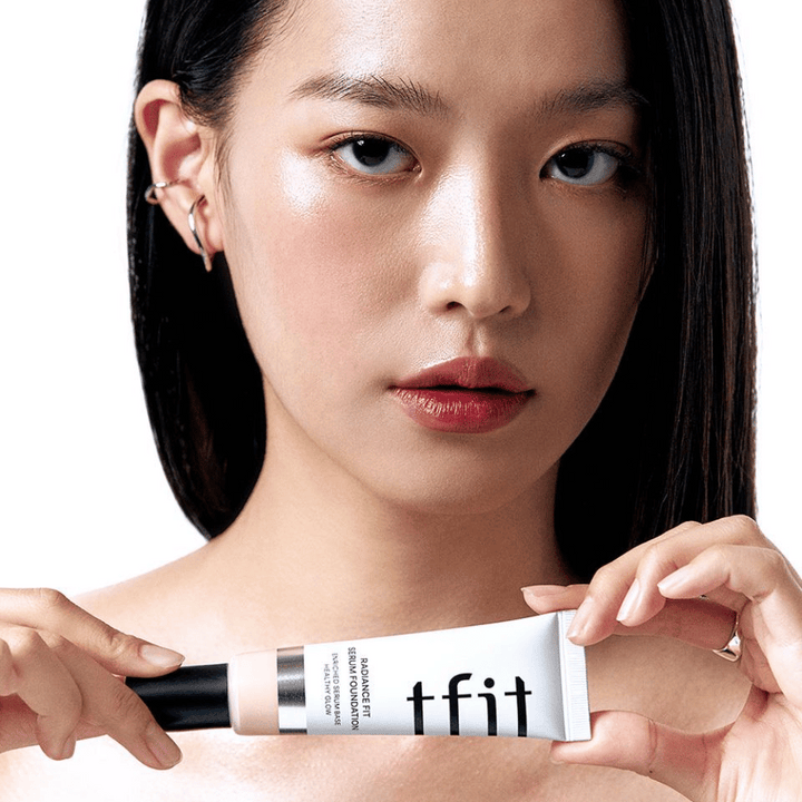 Modell med glansig, jämn hud håller i TFIT Radiance Fit Serum Foundation, vilket framhäver produktens naturliga finish och lyster.