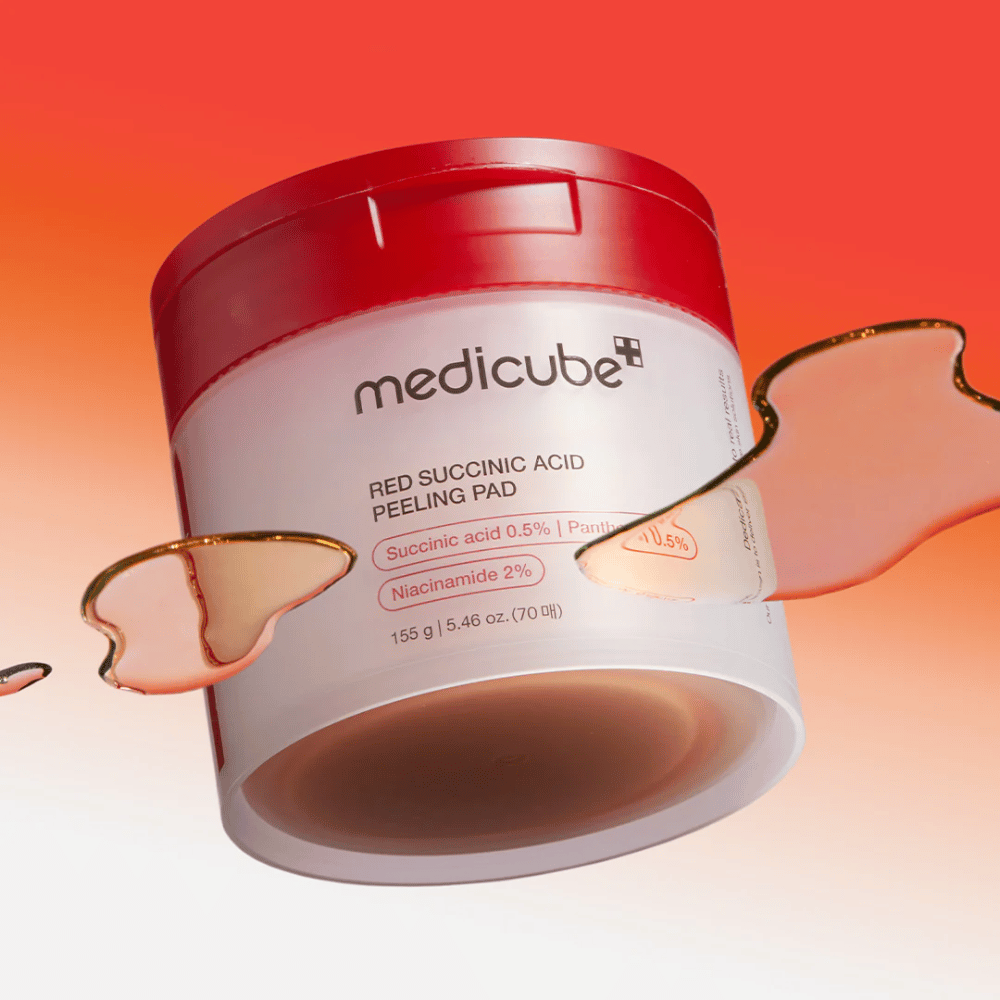 Medicube Red Succinic Acid Peeling Pad in een witte en rode pot, geplaatst tegen een gradiëntachtergrond in rood en oranje. Het product bevat succinylzuur en niacinamide voor exfoliatie en huidverbetering. Vloeibare textuur zichtbaar rond de pot.