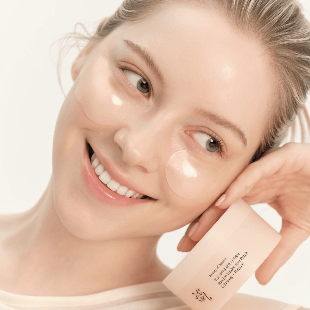 Model met Beauty of Joseon onder oogpatches en product in hand, oogpatches met ginseng en retinal voor een frissere en gladdere oogomgeving.