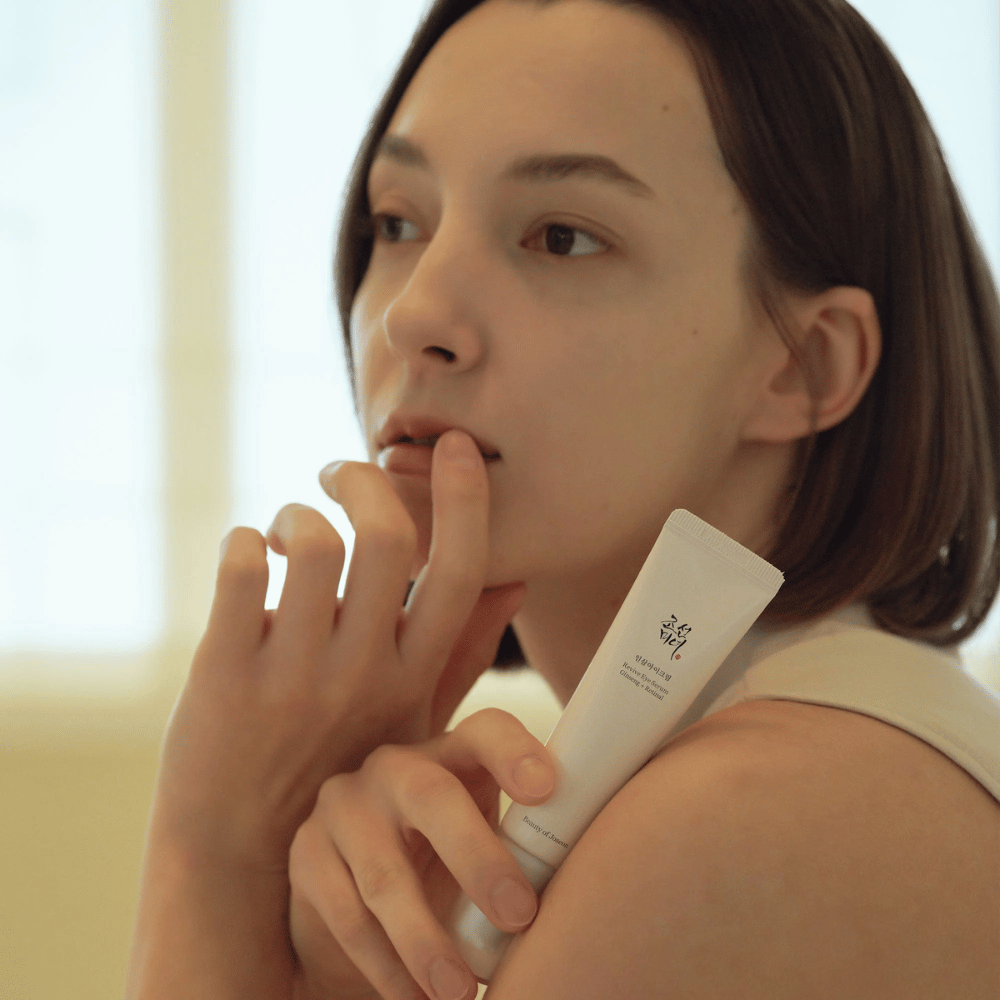 Model houdt Beauty of Joseon Revive Eye Serum vast en brengt voorzichtig aan op de huid voor een gehydrateerde en gladde oogcontour.