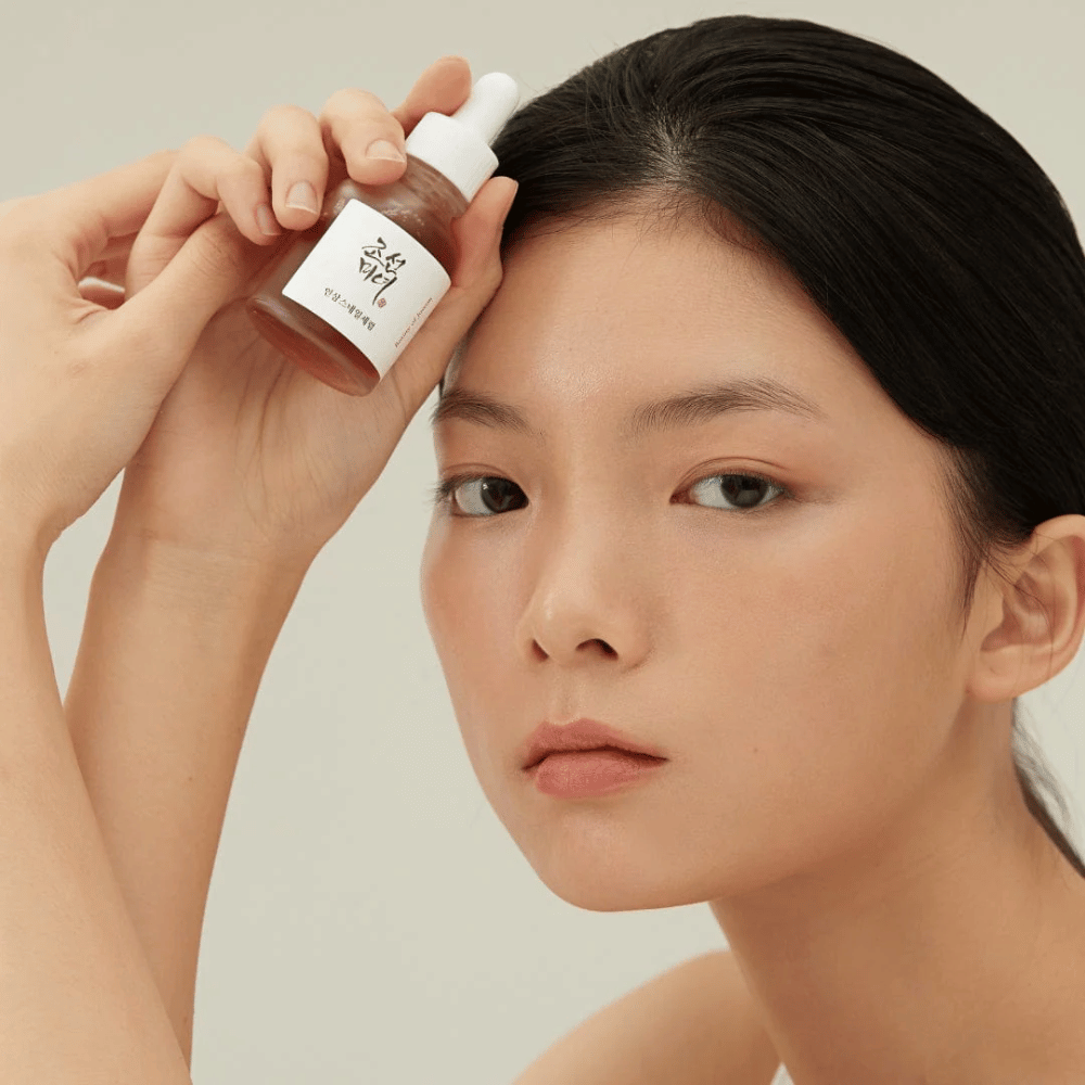 Model houdt Beauty of Joseon Revive Serum bij de wang – voedend serum met ginseng en snail mucin.
