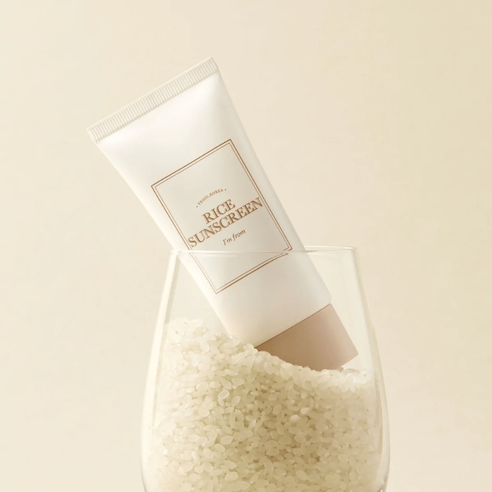 Tube met "I'm from" Rice Sunscreen, SPF50+ PA++++, geplaatst in een glas met rijstkorrels.