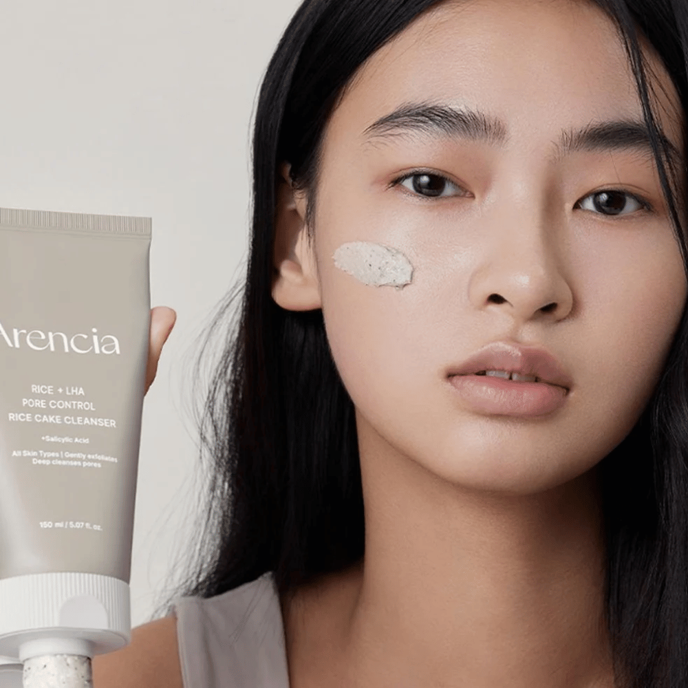 Model die Arencia Rice + LHA Pore Control Rice Cake Cleanser vasthoudt met aangebrachte product op de wang, illustreert milde maar effectieve poriënreiniging voor dagelijks gebruik.