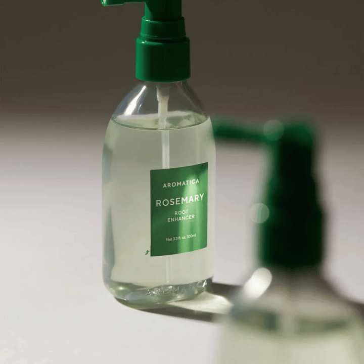 Close-up van AROMATICA Rosemary Root Enhancer met groen applicatormondstuk. De afbeelding focust op het ontwerp van de fles en de precieze applicatie direct op de hoofdhuid.