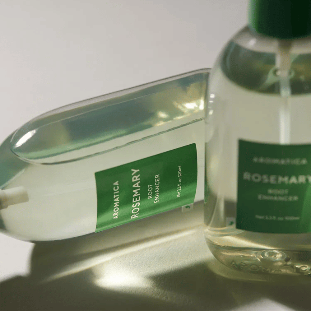 Twee AROMATICA Rosemary Root Enhancer-flessen met transparante beschermdop en groen etiket. Close-up die het premiumdesign van het product en het natuurlijke haarverzorgingsconcept benadrukt.