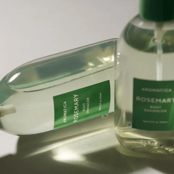 Twee AROMATICA Rosemary Root Enhancer-flessen met transparante beschermdop en groen etiket. Close-up die het premiumdesign van het product en het natuurlijke haarverzorgingsconcept benadrukt.