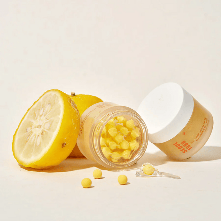 Öppen burk med gula kapslar bredvid halverad yuja-frukt som framhäver C-vitaminrik formula.