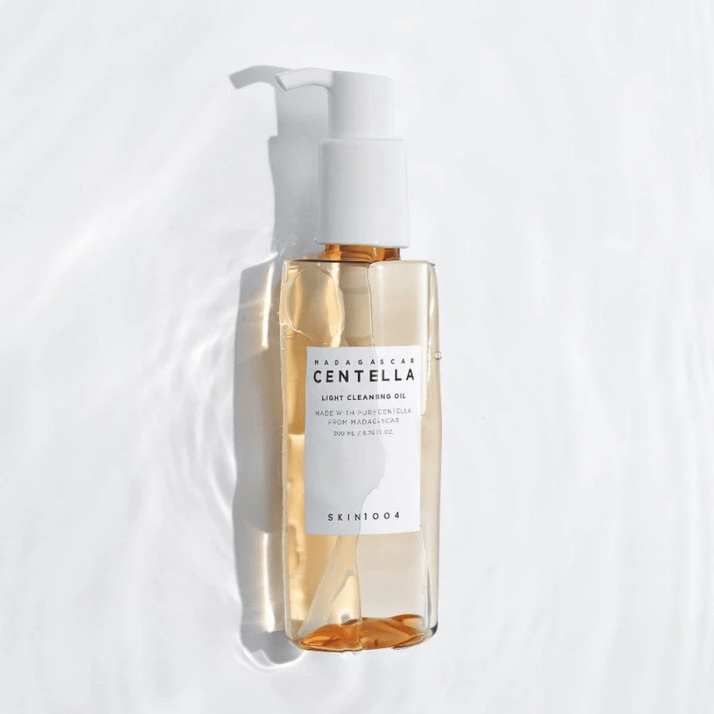 SKIN1004 Madagascar Centella Light Cleansing Oil op witte achtergrond met zachte waterreflecties die de transparante fles en gouden inhoud benadrukken.