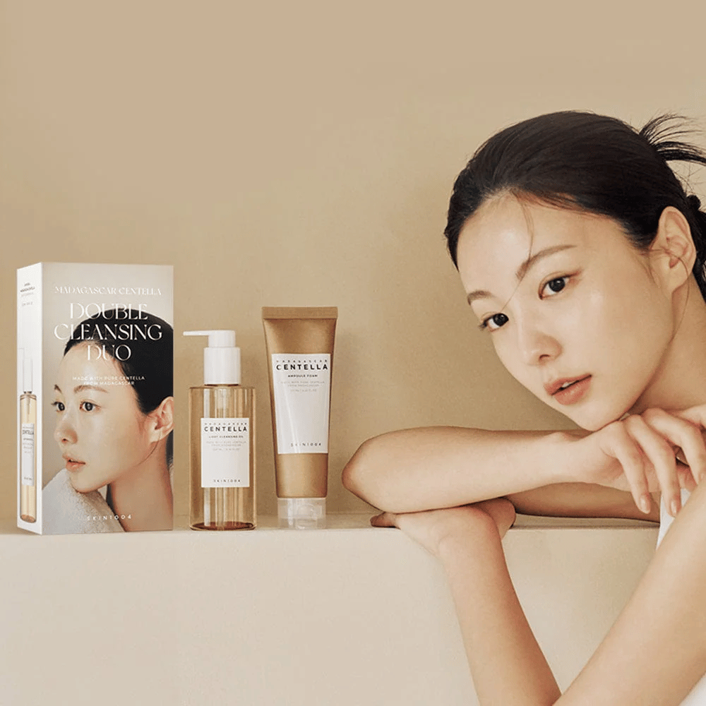 SKIN1004 Madagascar Centella Double Cleansing Duo Set met karton, oliebasisreiniging, schuimreiniging en model met gehydrateerde huid tegen beige achtergrond.