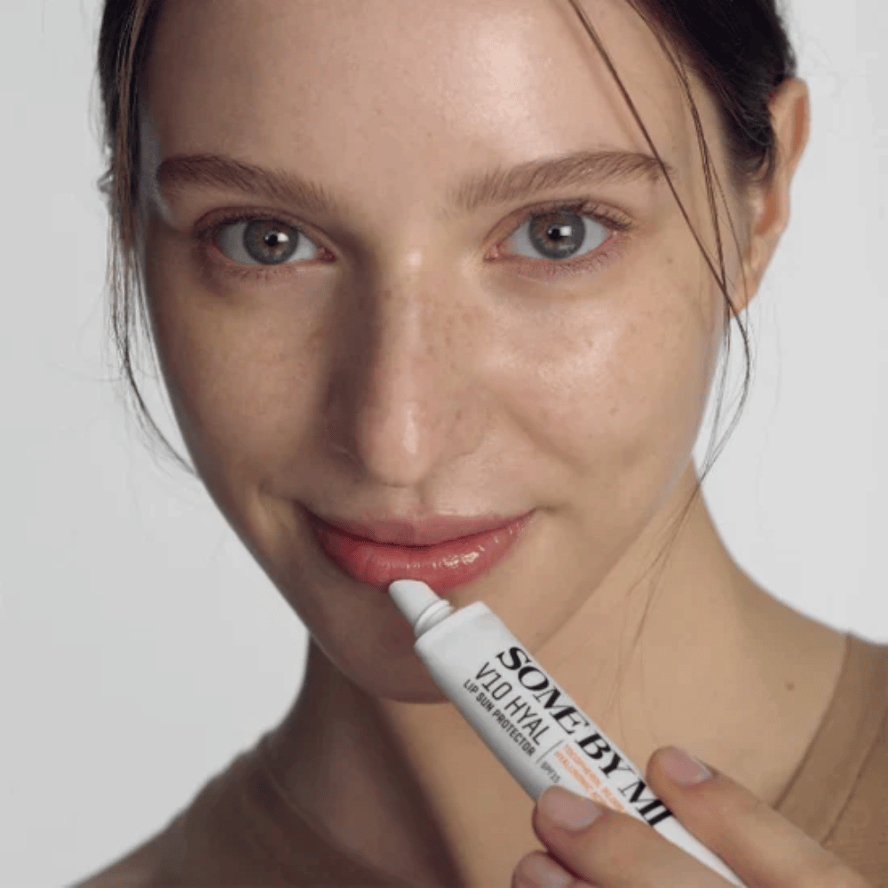 Een vrouw houdt een tube V10 Hyal Lip Sun Protector SPF15 7ml lippenbalsem voor zonnebescherming en hydratatie, van SOME BY MI.