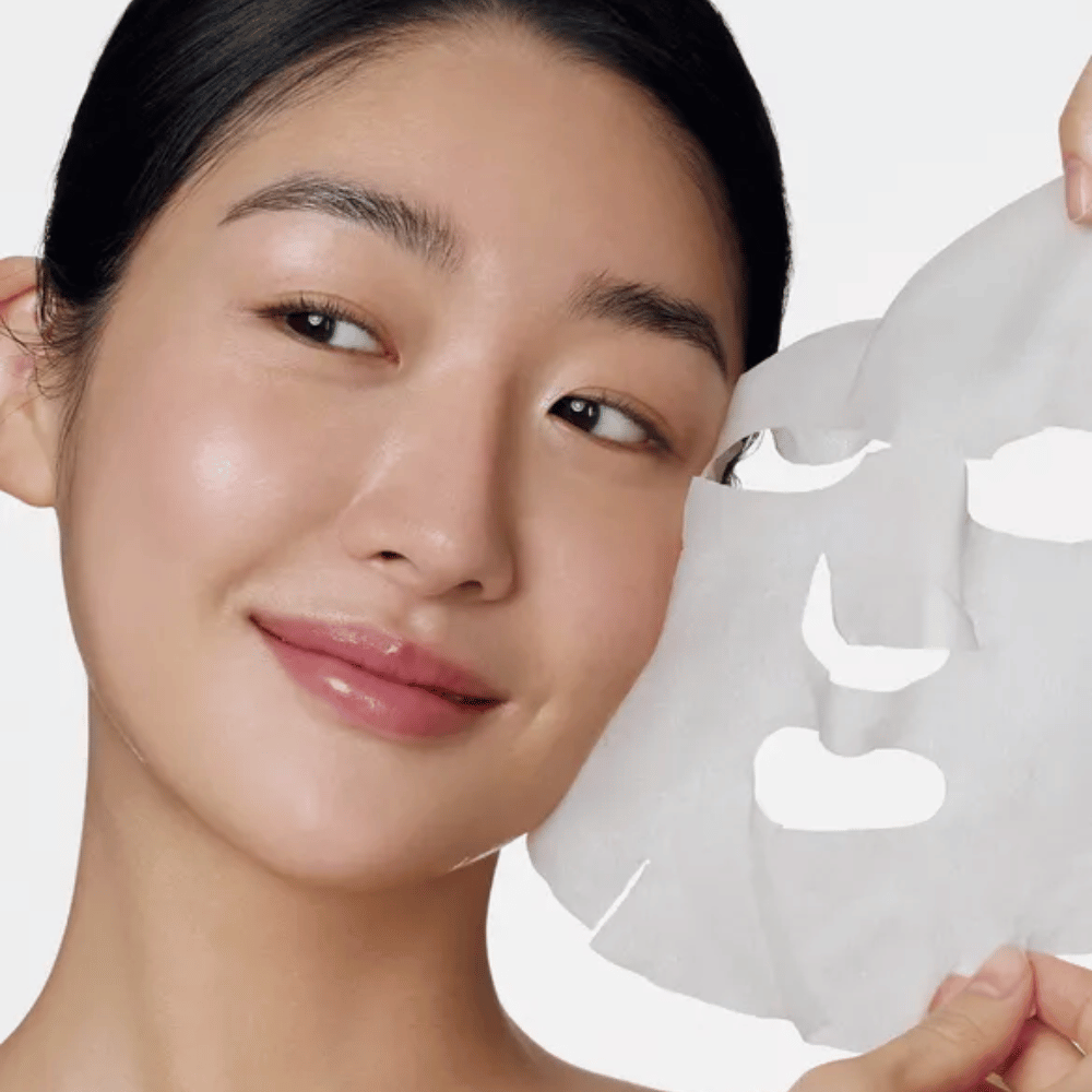 De afbeelding toont een persoon die een gezichtsmasker gebruikt, specifiek een "Retinol Intense Daily Mask" van Some By Mi. Het masker is ontworpen voor dagelijks gebruik en bevat retinol om de huidtextuur te verbeteren, fijne lijntjes te verminderen en een egalere huidtint te geven.