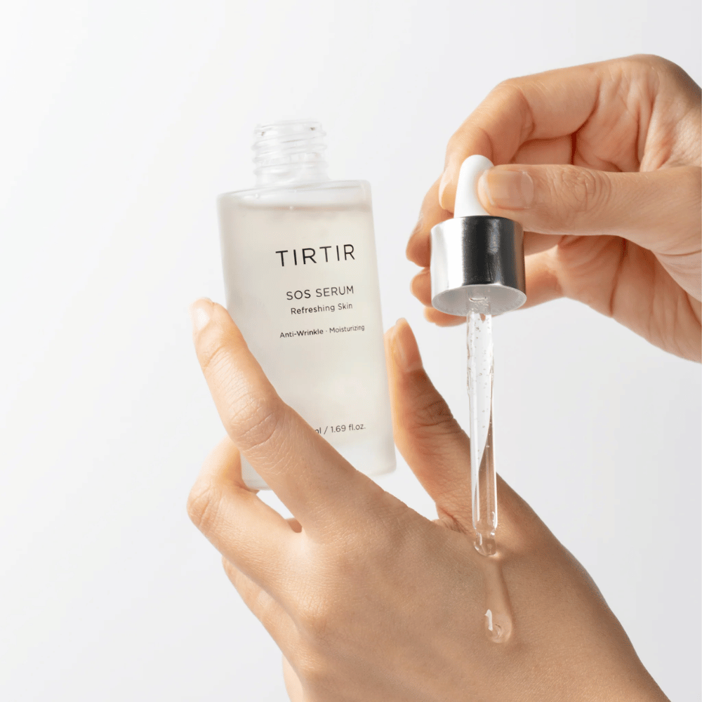 Handen die TIRTIR SOS Serum uit een pipet laten druppelen, bedoeld voor huidverzorging.