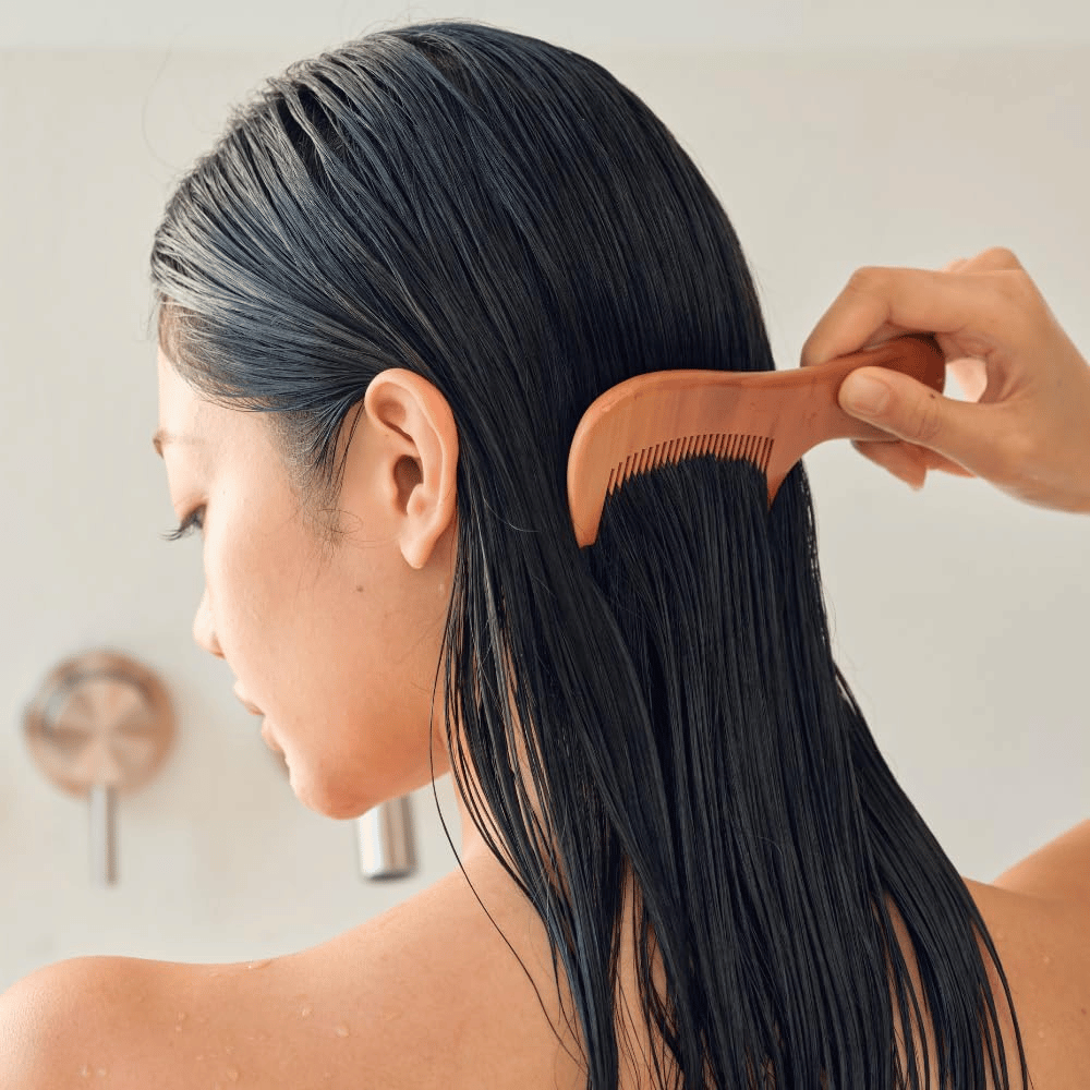 Persoon kamt lang, nat haar door met een brede kam na het aanbrengen van Heveblue Salmon Pullkeratin Centella Hair Treatment. Illustreert de ontwarrende en verzachtende werking voor een gladder resultaat.