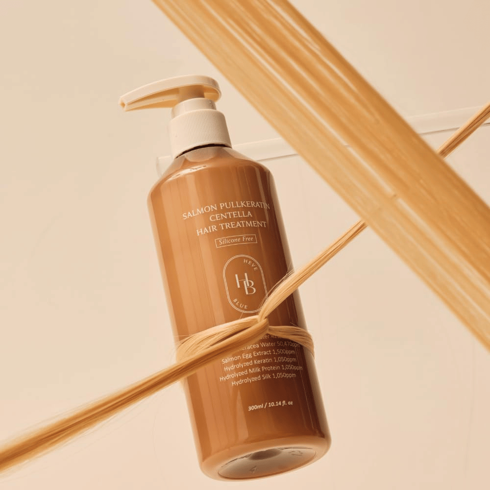 Heveblue Salmon Pullkeratin Centella Hair Treatment in bruine fles omringd door haarlokken. De afbeelding benadrukt de verzorgende eigenschappen van de haarbehandeling met focus op glans, sterkte en zijdezacht haar.
