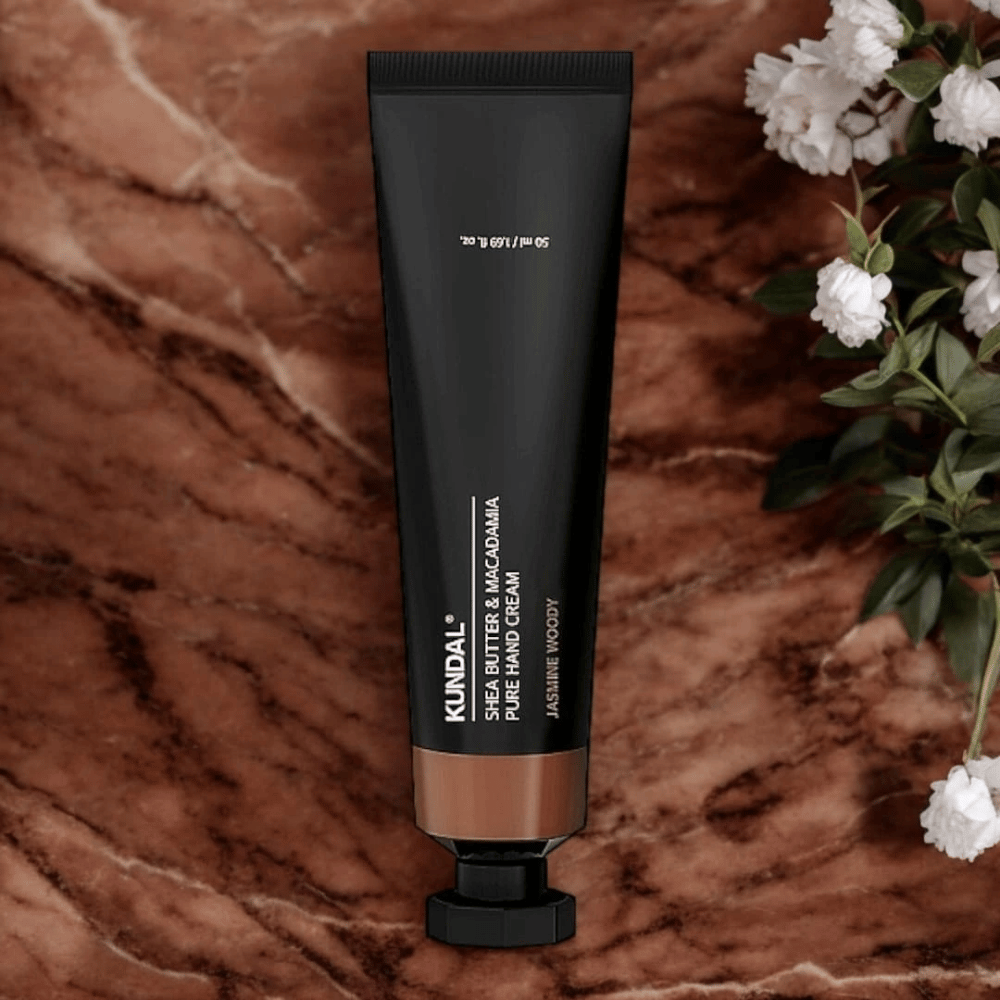 KUNDAL Shea Butter & Macadamia Pure Hand Cream Jasmine Woody geplaatst op marmer met bloemen – voedende handcrème die droge handen verzorgt en een elegante jasmijnhoutachtige geur geeft.