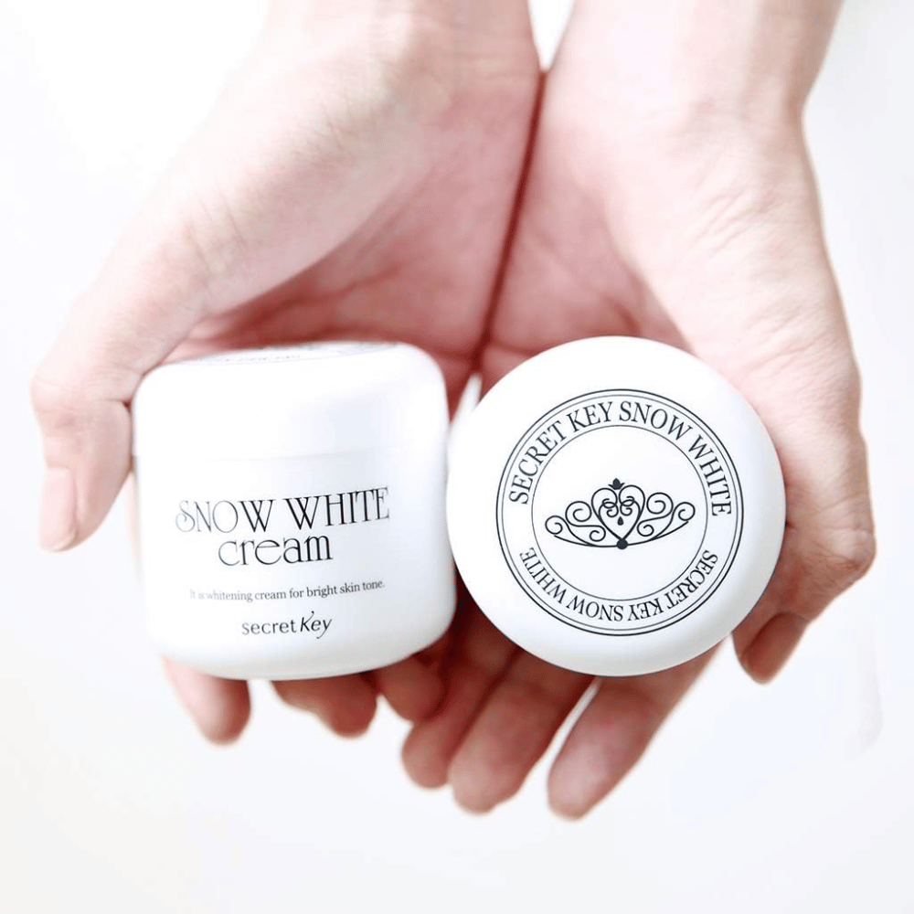 Twee potten Secret Key Snow White Cream worden in de handen gehouden, een toont het deksel en een toont de voorkant.