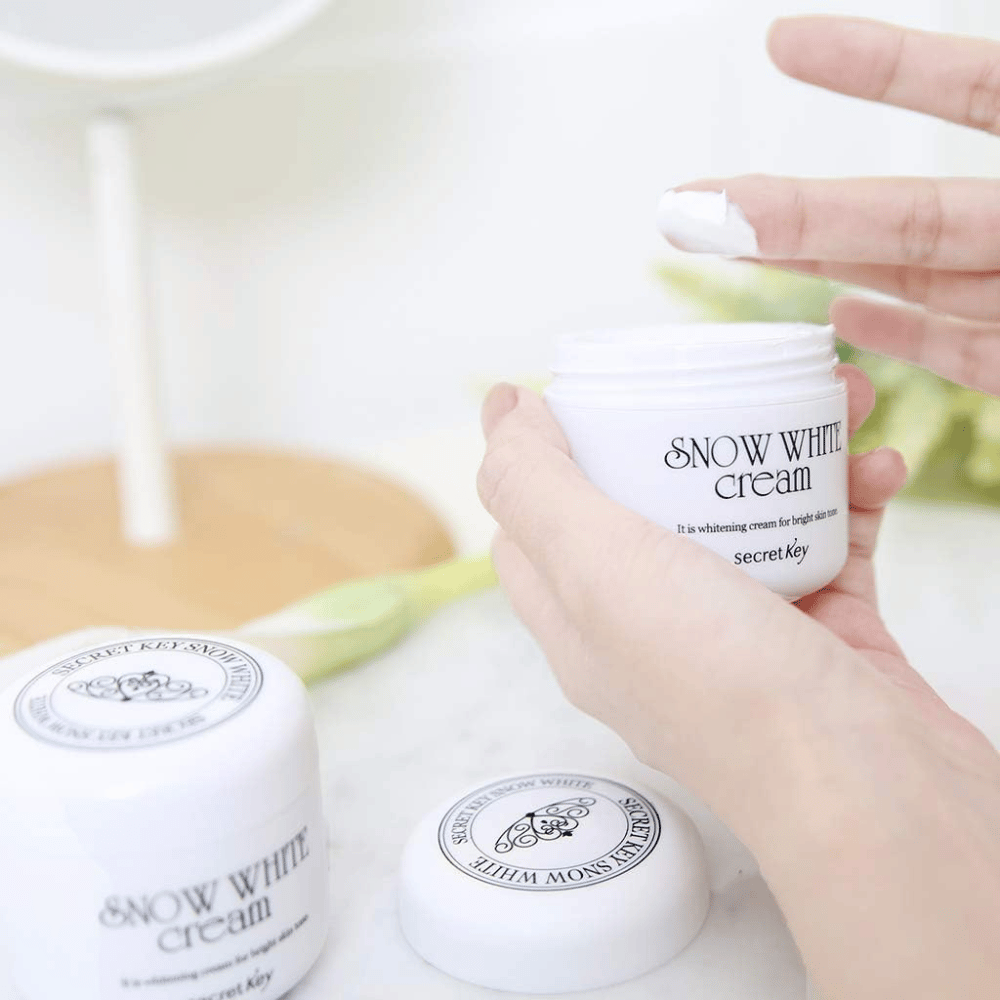 Hand die witte crème uit een pot Secret Key Snow White Cream op een make-uptafel neemt.
