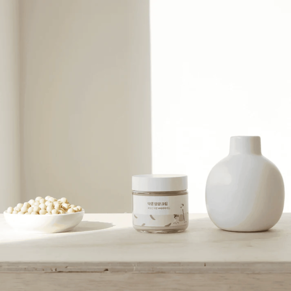 Mixsoon Soybean Nourishing Cream staat op een houten tafel naast een vaas en sojabonen. Een minimalistische, hydraterende crème met natuurlijke ingrediënten.