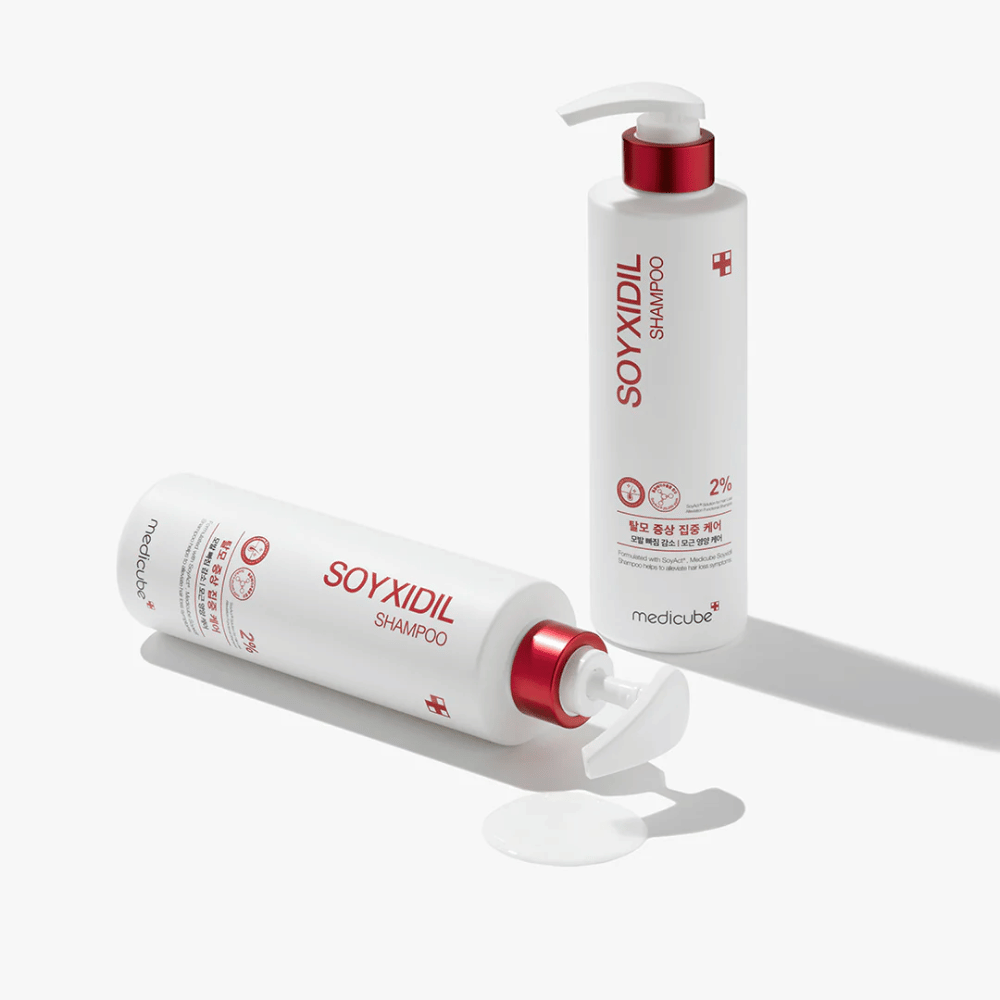 Twee flessen van Medicube Soyxidil Shampoo in wit en rood design, één staand en één liggend met gemorste shampoo ernaast.
