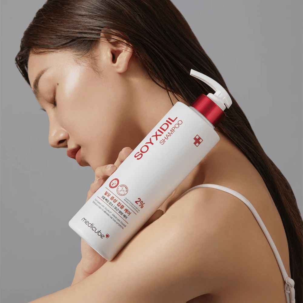 Vrouw met lang haar leunt haar hoofd tegen een fles Medicube Soyxidil Shampoo, die de hoofdhuid versterkt en haaruitval tegengaat.