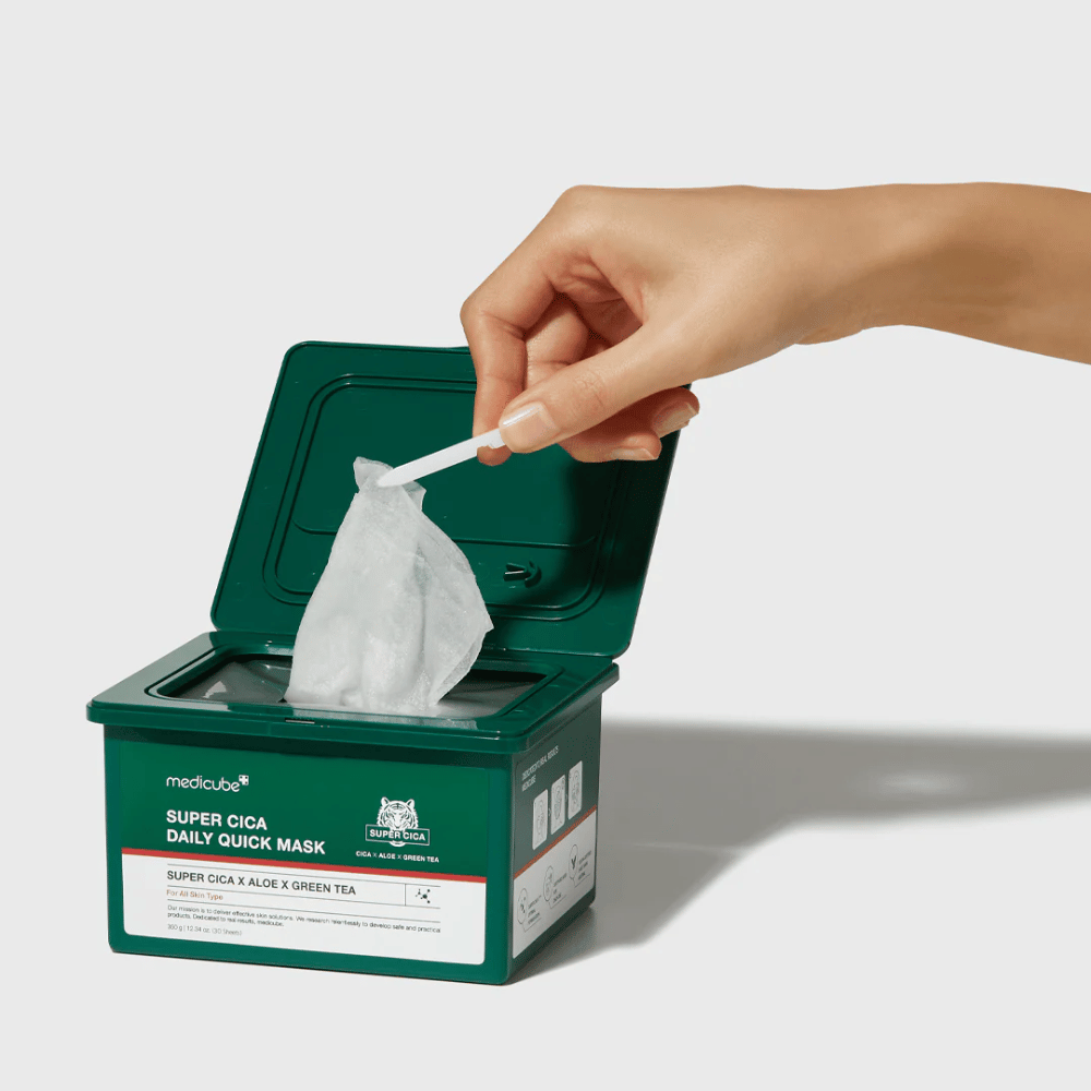 Groene houder met open deksel toont medicube Super Cica Daily Quick Mask. Een hand haalt een velmasker omhoog met bijgeleverde pincet. Het product bevat Cica, aloë en groene thee, ideaal voor snelle hydratatie en kalmerend effect.