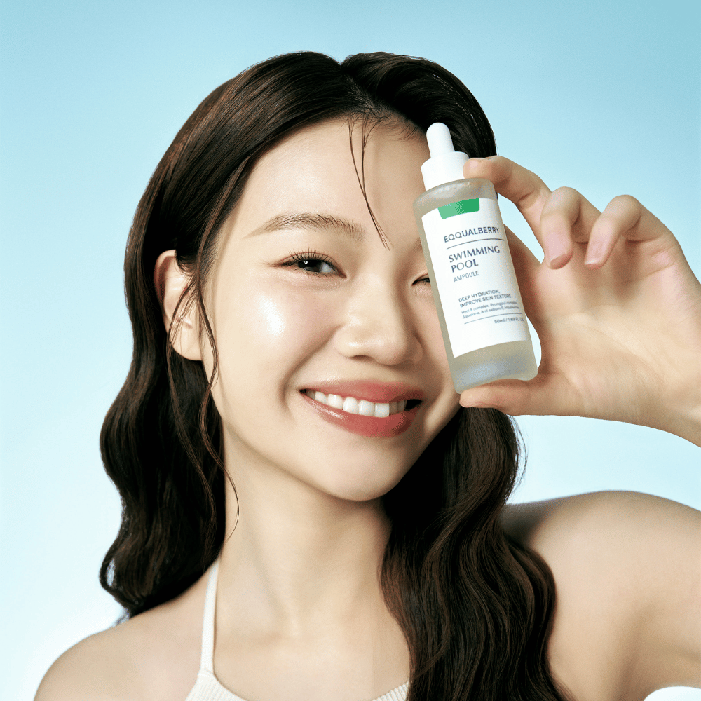 Een lachende vrouw houdt Eqqualberry Swimming Pool Ampoule omhoog, een huidverzorgingsproduct voor intensieve hydratatie, voor een lichtblauwe achtergrond.