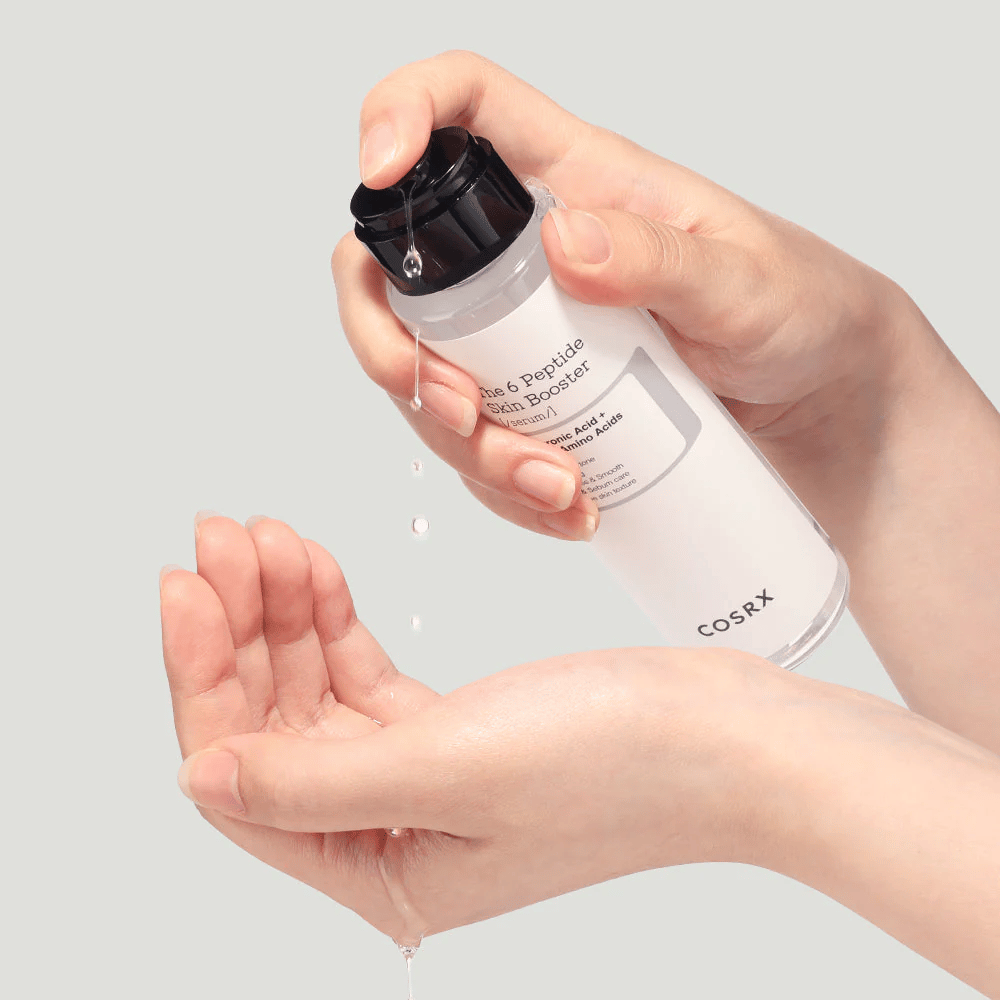 Handen die huidverzorgingsproduct uitgieten uit een doorzichtige fles met de tekst "The Peptide Skin Booster".
