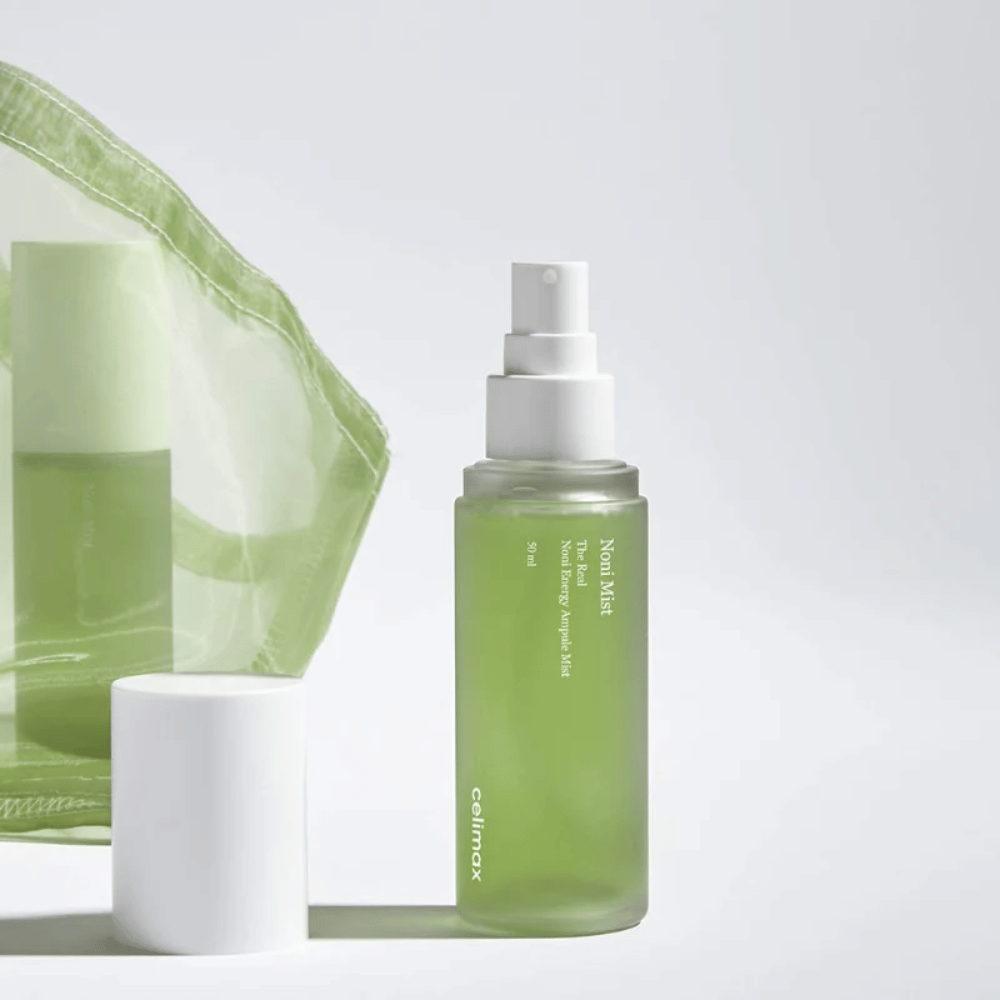 Een fles met Celimax Noni Mist, een groene spuitfles met witte pomp, die naast een dop staat. Het product is verpakt in een doorzichtige plastic zak en wordt gepromoot als Noni Energy Ampule Mist.